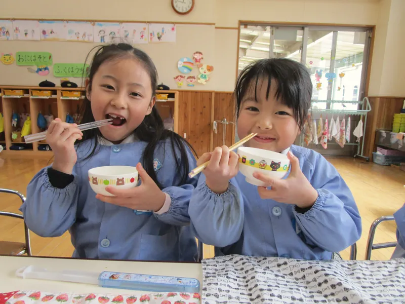 お茶わんを手に笑顔で食事する園児